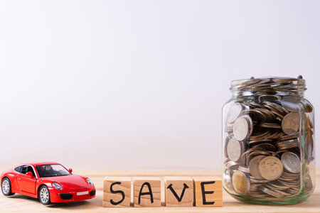 Wooden block stack with save word and jar full of coins and red car isolated grey background. Saving money and investment concept.の写真素材