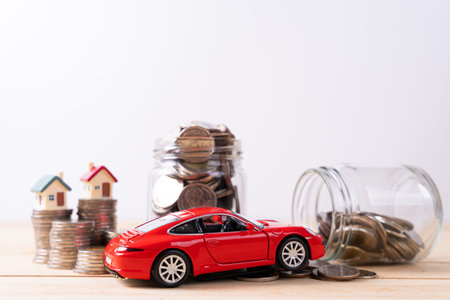 Jar full of coins with stack coin and red car on wooden table isolated grey background. Saving money...