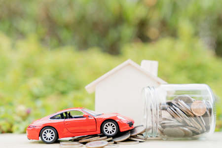 Jar of coins and red car on pile of coin on blurred green natural background. Saving money and investment concept.の写真素材