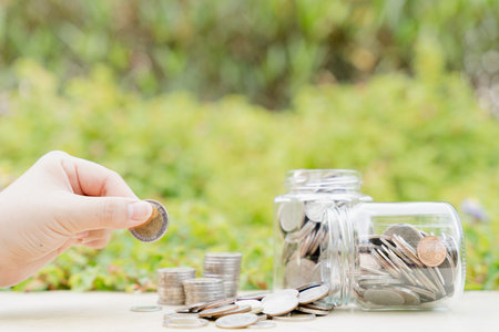 Hand put money coin into jar on blurred green natural background. Saving money and investment...