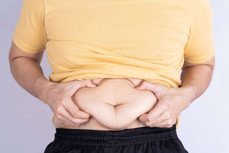 Fat man holding excessive fat belly isolated grey background.の写真素材