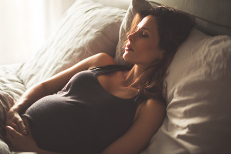 Pregnant woman rests peacefully on soft pillows, feeling her baby bump.の素材