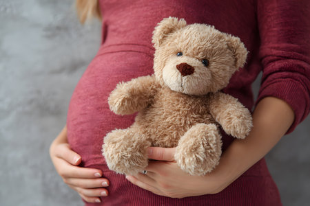 Pregnant belly holding soft teddy bear toy awaiting new life.の素材