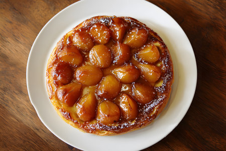 A golden tarte Tatin sits on a white plate showing fruit filling.の素材