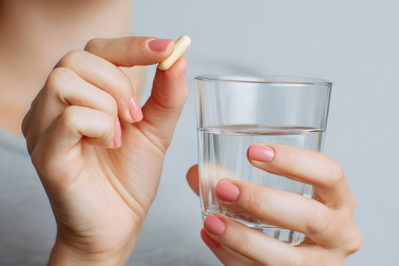 A hand holds a pill and a glass of water.の素材