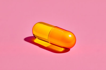 A single orange pill lays on a pink surface with shadow.の素材