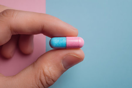 A hand holds a pink and blue pill against a pastel background.の素材