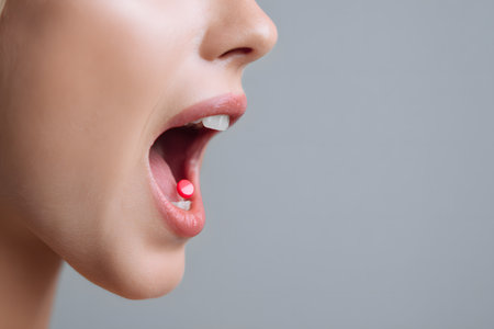 A red pill rests inside an open mouth about to be swallowed.の素材