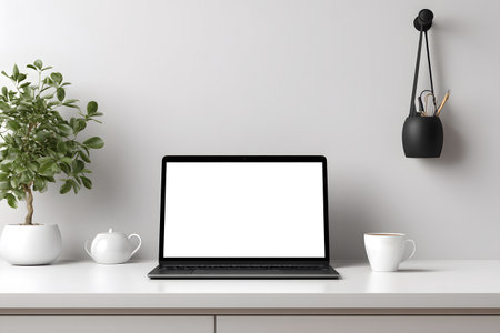 A laptop sits open on a desk next to a plant and a cup.の素材