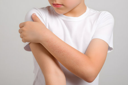 Child's arm showing rash and skin irritation, holding shoulder in discomfort.の素材