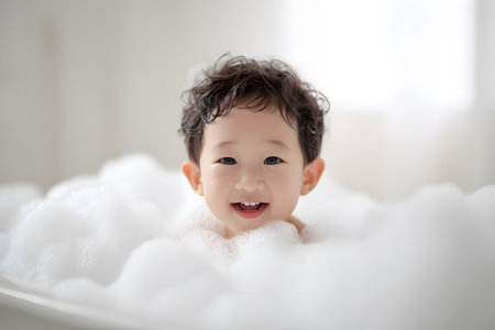 Baby smiles while playing in a bath filled with soft white bubbles.の素材