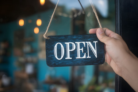 A hand holds a sign that says open in front of a blurred background.の素材