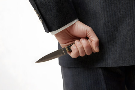 A hand holds a knife hidden behind a suit jacket.の素材