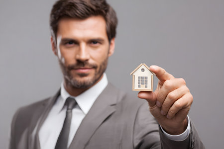 A person shows a small house in their hand representing home ownership.の素材