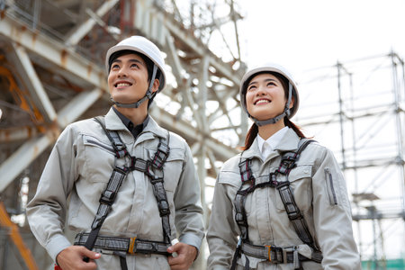 Workers wear helmets and harnesses for safety while looking up.の素材