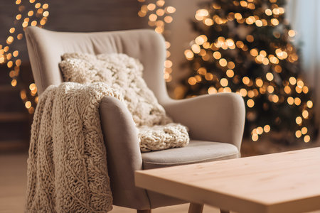 A cozy chair with blankets sits near a decorated Christmas tree glowing with warm lights.の素材