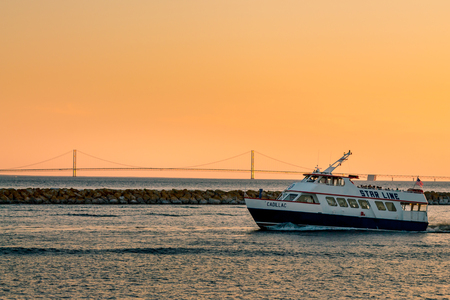 Star Line ferry leaving Mackinac Island harbor in front of the Mackinac Bridge at sunsetのeditorial素材
