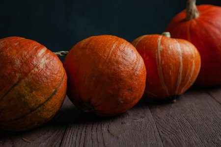 Four pumpkins in a row on wooden table in dark mood.