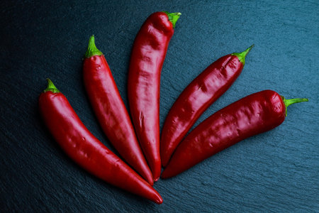 Five chilli peppers on black slate board. Flat lay.