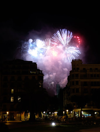 Fireworks breaking through a smoke filled sky above lit up streets causing silhouettes of buildings.の写真素材