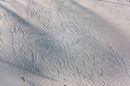 Snowy off-piste ski slope with traces of skis and snowboards on a winter dayの写真素材