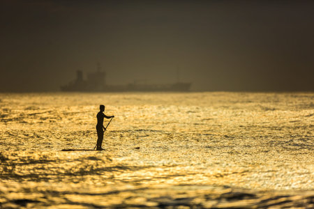 Silhouette of a surfer standing on a paddleboard waiting for a big wave at dawn