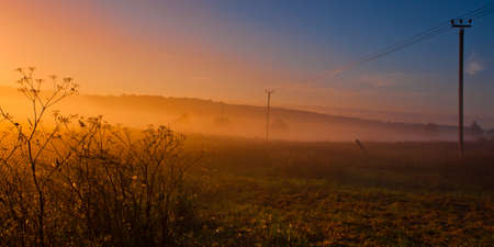 Fog on the countryside, next to the poles with wires, orange glowing fog, bright colors, photo panoramaの写真素材