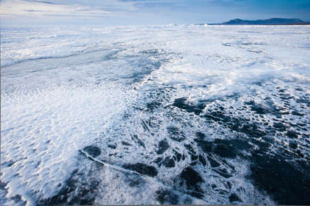 Snow and ice on the flat surface of Lake Baikal under a blue sky in the distance mountain rangeの写真素材