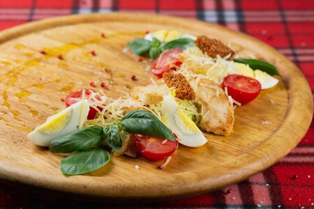 Caesar salad with juicy chicken egg and fresh vegetables on a wooden boardの写真素材