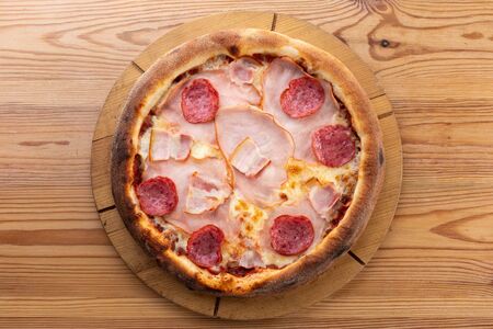 hearty italian pizza on a wooden board. crispy pizza with ham, bacon, salami and cheese sausagesの写真素材