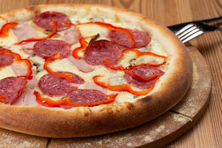 hearty italian pizza on a wooden board. crispy pizza with ham, pepper, salami and cheese sausagesの写真素材