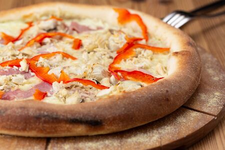 hearty italian pizza on a wooden board. pizza with chicken, pepper, ham and cheeseの写真素材