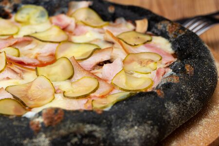 hearty italian pizza on a wooden board. black crispy cheese pizza with ham, selensi cucumbers and mushroomsの写真素材