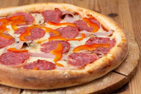 hearty italian pizza on a wooden board. 
pizza with salami, fresh pepper and hamの写真素材