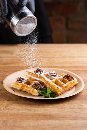 Viennese waffles on a disposable plate with peanut butter, icing sugar and mint. chef decorates dessert with powdered sugarの写真素材