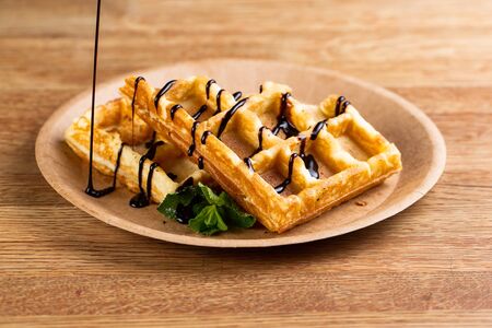 Viennese waffles on a disposable plate with liquid chocolate, icing sugar and mint. cook pours liquid chocolate for dessertの写真素材