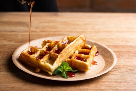 Viennese waffles on a disposable plate with strawberry jam and mint. chef pouring fruit jam for dessertの写真素材