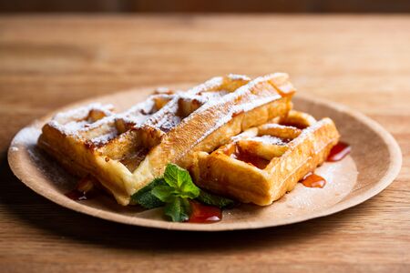 Viennese waffles on a disposable plate with strawberry jam, icing sugar and mint. cook decorates dessert with icing sugarの写真素材