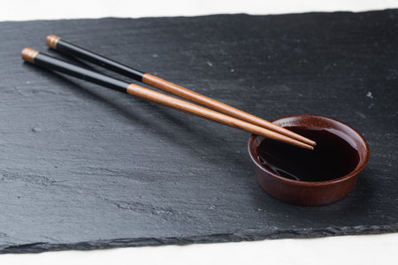 Black board on a white background. Empty black granite stone rectangular board on white textured background. sushi sticks and soy sauce on coasters on a stone boardの写真素材