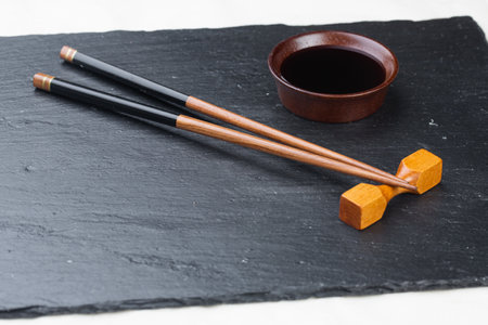 Black board on a white background. Empty black granite stone rectangular board on white textured background. sushi sticks and soy sauce on coasters on a stone boardの写真素材