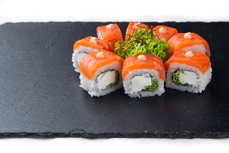 Sushi roll with salmon, avocado and cheese on a black stone plate on a white plate. Sushi menu. Japanese food.の写真素材