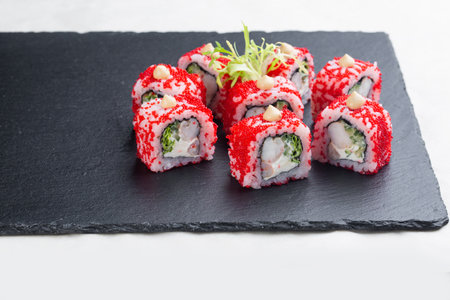 Sushi roll with salmon, red avocado caviar and cheese on a black stone plate on a white plate. Sushi menu. Japanese food.の写真素材
