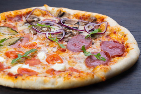 Delicious italian pizza with fresh tomatoes, olives, onions, sausage, ham and basil on an old wooden boardの写真素材