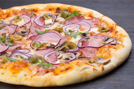 Delicious italian pizza with fresh tomatoes, olives, onions, sausage, ham and basil on an old wooden boardの写真素材