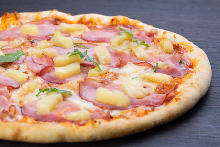 Delicious italian pizza with fresh tomatoes, pineapples, olives, ham and basil on an old wooden boardの写真素材