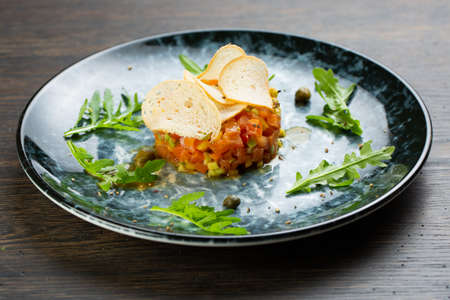 salmon tartare with pepper and tomatoes. fish tartare with thin slices of white bread on a blue mnamoreny plateの写真素材