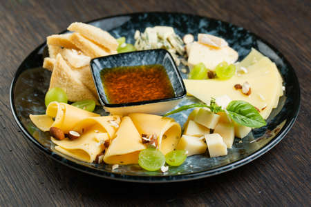 cheese plate with green grapes, crunchy croutons and nuts. set of different types of cheese with honey on a marble plateの写真素材