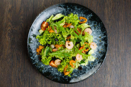 salad of shrimp, fresh cucumber and cherry tomatoes, Chinese cabbage and olives. salad dressed with olive oil. fish salad on a blue marble plate. view from aboveの写真素材