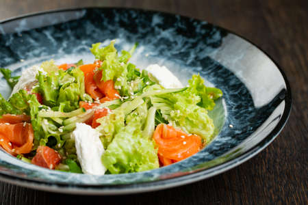 Greek salad of tomatoes, pickled peppers, cucumbers, lettuce and feta cheese. greek salad with olives and white sesame seeds on a blue marble plateの写真素材