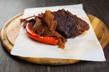 spicy meat chips with red pepper. dried, marinated beef and pork on a wooden plate. beer snackの写真素材